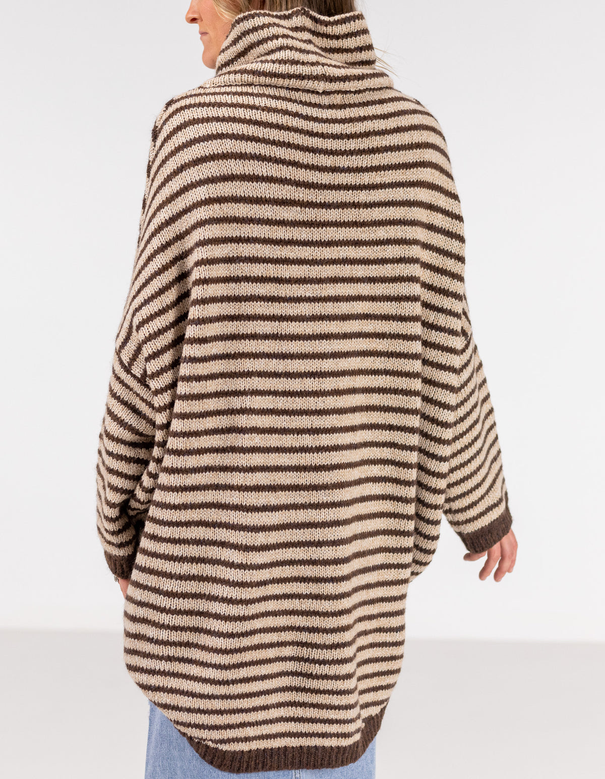 Rear half-body shot showing the extended back drape of the chocolate and beige stripe jumper over a denim skirt.