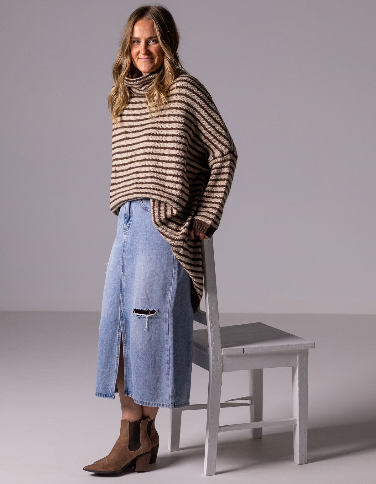 Full-length view of the oversized chocolate and beige stripe jumper styled with a denim midi skirt and boots.