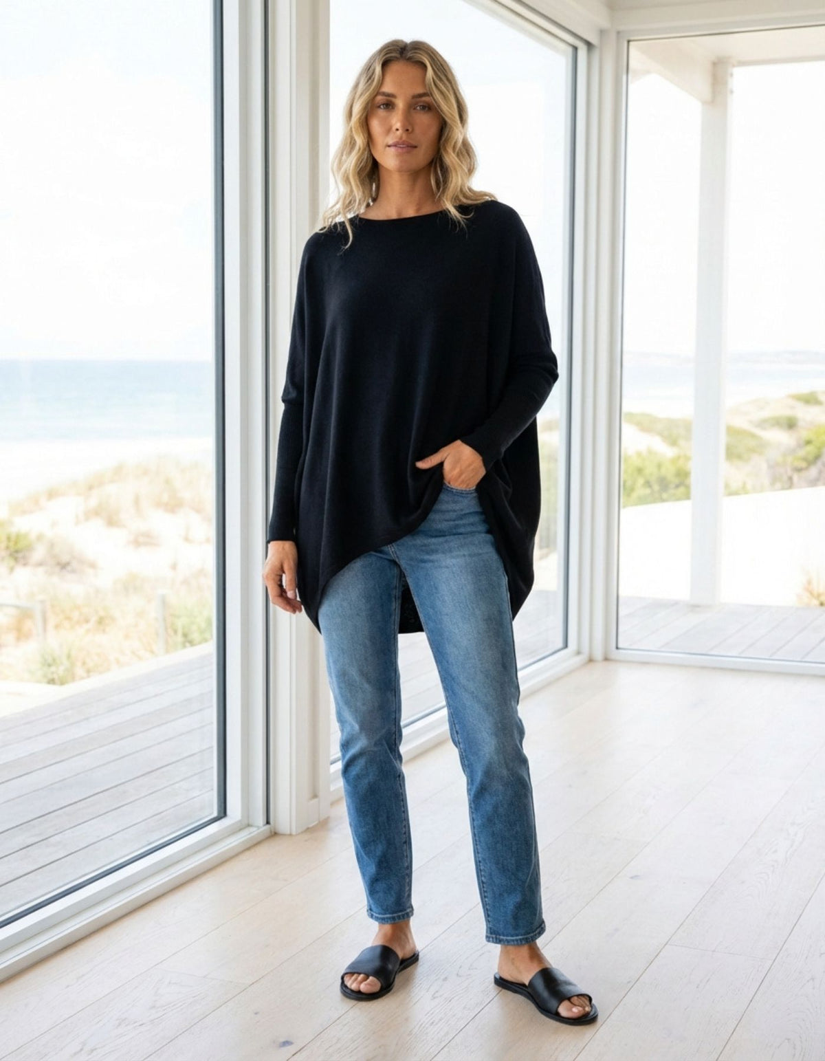 Full body styling of the black knitwear piece highlighting the relaxed fit torso, ribbed sleeves, and blue jeans.