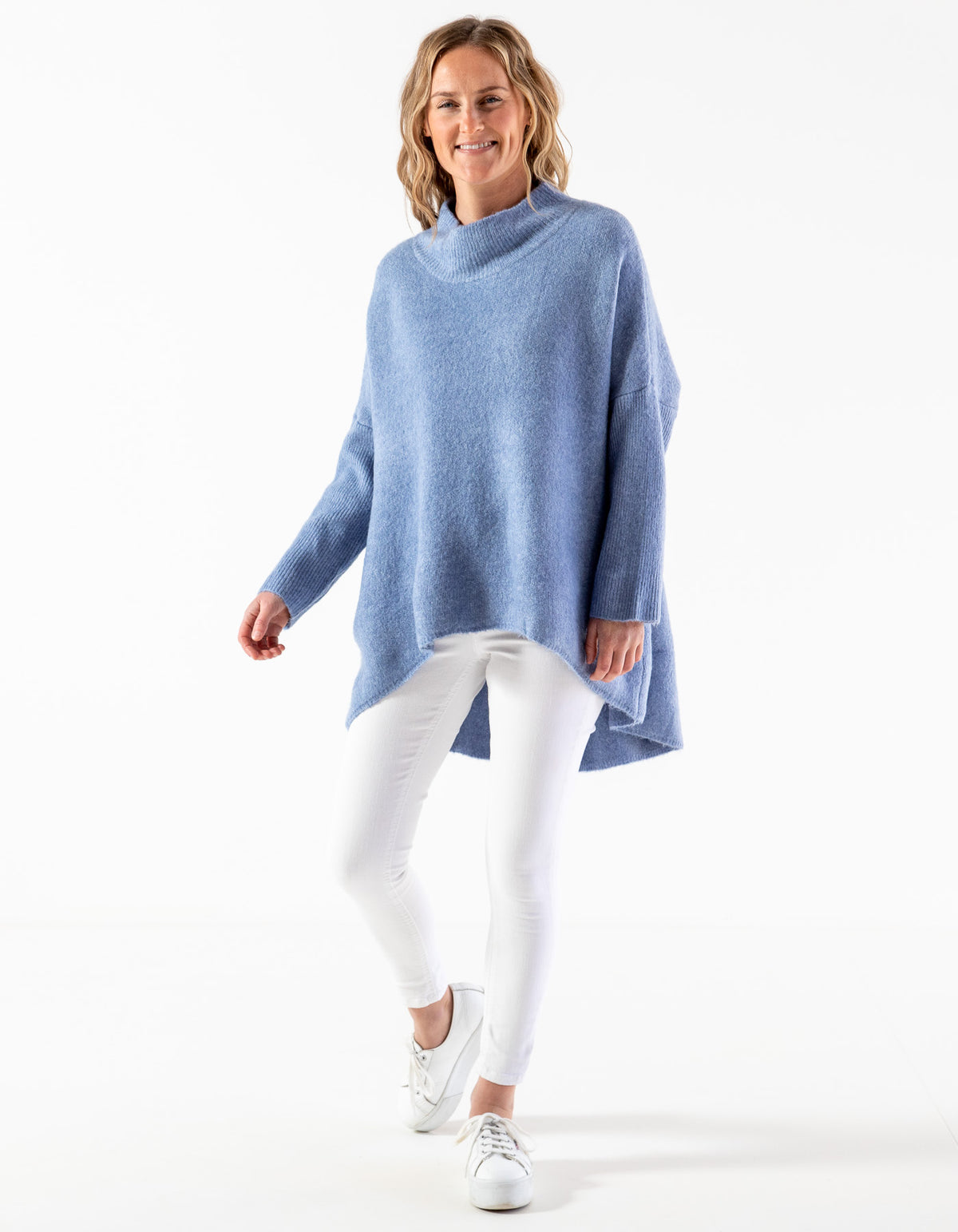 Full-length view of the Karma Kameleon blue oversized jumper styled with white pants and sneakers.
