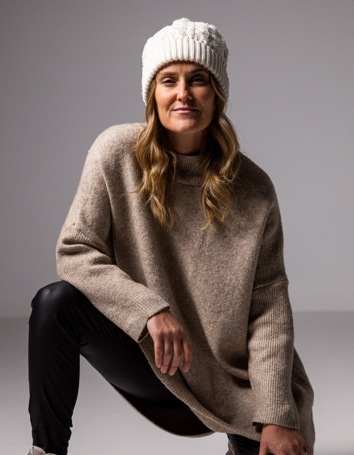 Full-body shot of the beige brushed knit jumper highlighting the ribbed funnel neck and sleeves.