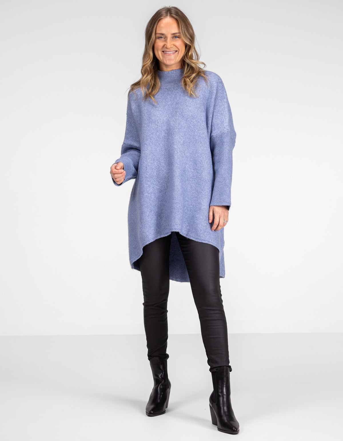 Full-length view of the oversized blue knitwear highlighting the hi-low hemline over black pants.
