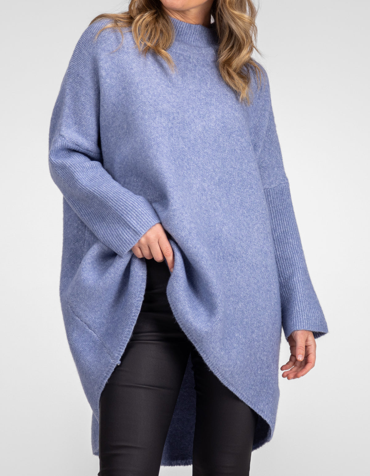 Front half-body shot of the Karma Kameleon blue knit jumper highlighting the oversized torso over black pants.