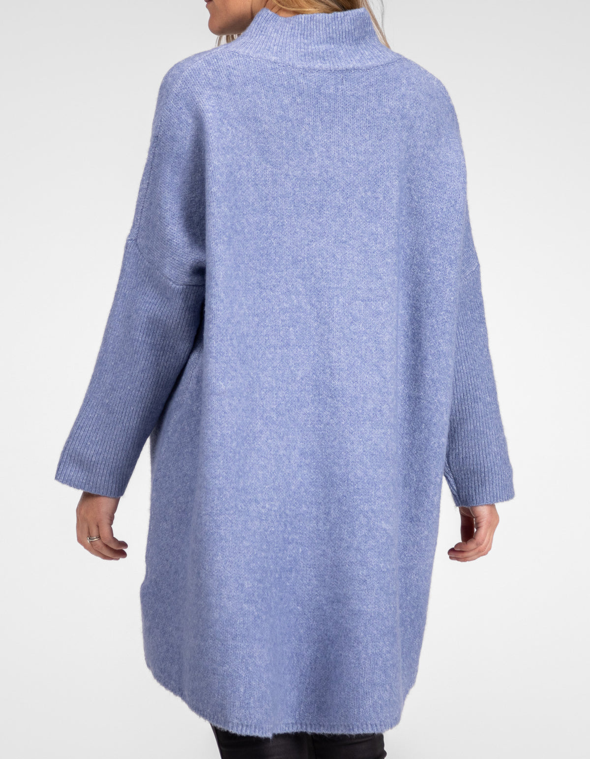 Rear angle view showing the extended back drape of the blue knit jumper over black pants.