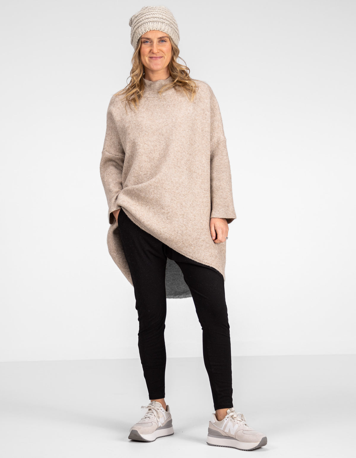 Full-length view of the oversized beige knitwear showcasing the relaxed drop shoulders with black pants and sneakers.